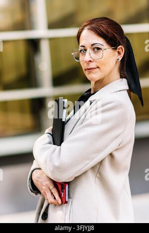 Donna d'affari sicura di sé con occhiali che porta un tablet e uno smartphone Foto Stock