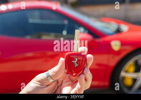 Ljubljana, Slovenia - 4 agosto 2026: Una persona tiene una chiave rossa della Ferrari mentre è in piedi vicino a un'automobile sportiva rossa. Foto Stock