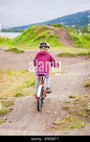Bambino visto di spalle che pedala su una pista sterrata con colline, Are, Jämtland, Svezia Foto Stock