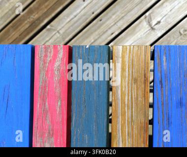 Panne di legno consumate in tonalità di blu, rosa e giallo creano una panchina vivace in contrasto con il deck diagonale in legno naturale, mostrando la texture a Foto Stock