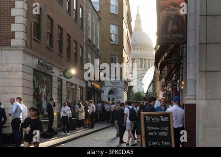 Le folle dell'ora di pranzo si godono bevande fuori dal Wren Tavern su Olde Watling Street, Londra, incorniciate dalla Cattedrale di San Paolo. Foto Stock