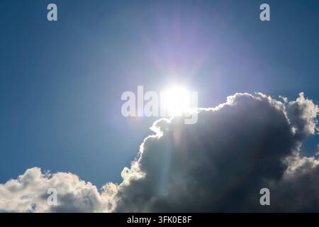 Raggi di sole che emergono da dietro una nuvola scura contro un cielo blu vibrante Foto Stock