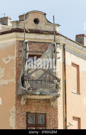 Facciata storica erosa con un balcone danneggiato, muratura a vista, intonaco scrostato e supporti metallici. Foto Stock