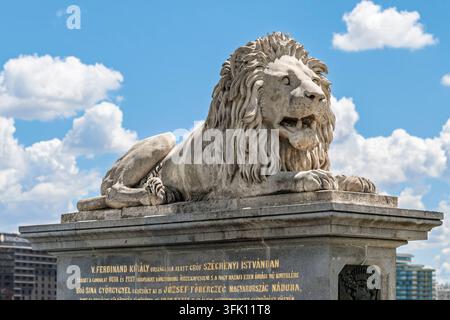 Una scultura in pietra calcarea scolpita a forma di leone con criniera fluente giace su un piedistallo all'ingresso del Ponte delle Catene, con la bocca aperta e le zampe dettagliate a riposo Foto Stock