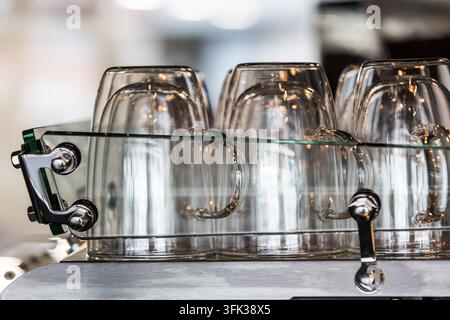 Tazze da caffè in vetro a doppio strato sono posate sul riscaldatore della macchina per l'espresso in un caffè specializzato, tenendole preriscaldate per una preparazione ottimale. Foto Stock