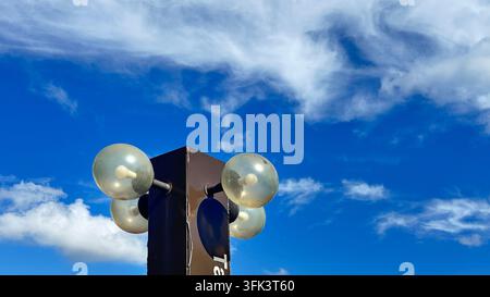 Una lampada da esterno marrone scuro a più globi o supporto su un cielo blu brillante con nuvole sottili. Foto Stock