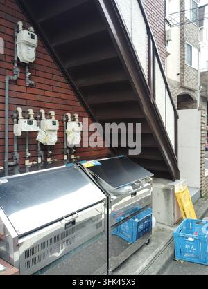 Contatori del gas, contenitori di stoccaggio comuni per i rifiuti e cassette di riciclaggio davanti a un edificio residenziale a Tokyo, Giappone. Foto Stock