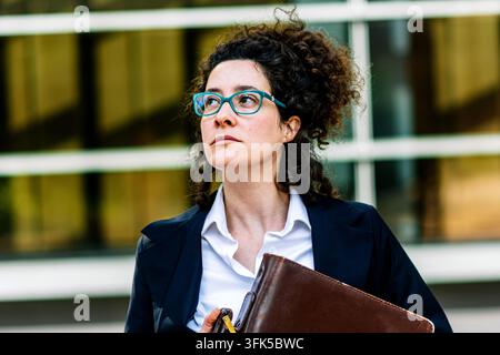 Donna d'affari sicura di sé con occhiali, che porta una valigetta e guarda avanti Foto Stock