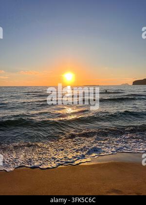 Un nuotatore solitario si gode il bagliore dorato del tramonto sulle onde gentili della spiaggia di Phalasarna, con la schiuma del mare che si riversa sulla sabbia, Creta. Foto Stock