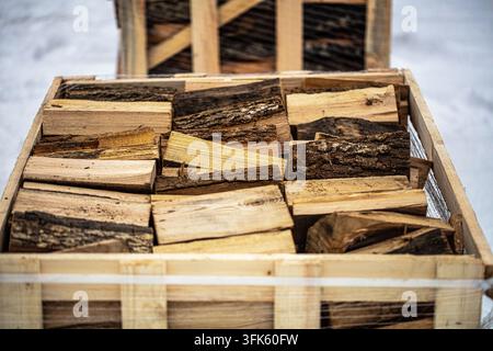 Vista di una cassa di legno piena di pezzi di legna da ardere ordinatamente impilati, con la neve visibile sullo sfondo, Lettonia. Foto Stock