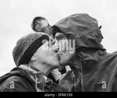 Coppia di anziani affettuosi in giacca antipioggia e berretto di lana che si baciano all'aperto Foto Stock