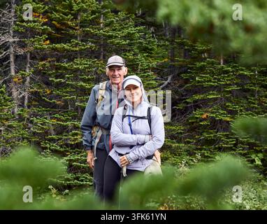 Ritratto di una figlia sorridente e di un padre anziano che fanno escursioni tra gli alberi nel bosco, Waterton Lakes National Foto Stock