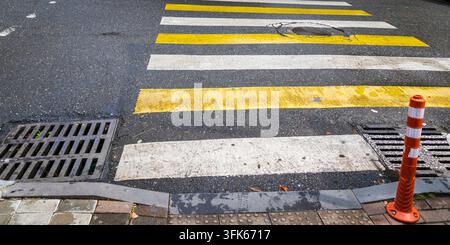 Vista ad angolo alto di un passaggio pedonale con strisce alternate gialle e bianche su una strada asfaltata urbana. Foto Stock
