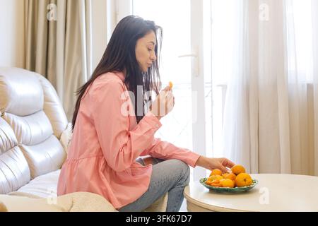 Donna bruna che mangia mandarini a casa Foto Stock