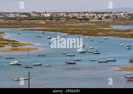 Vista sulle piccole barche ormeggiate nella laguna della Ria Formosa con lo skyline della città di Faro sullo sfondo, Faro, distretto di Faro, Portogallo. Foto Stock