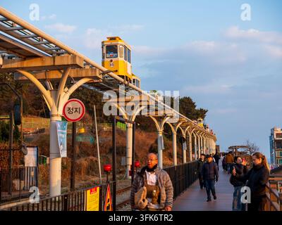 Busan, Busan, Corea del Sud - 14 febbraio 2026: Vista del treno della spiaggia di Haeundae e della capsula Sky al Blueline Park con persone che camminano lungo il pontile di legno Foto Stock