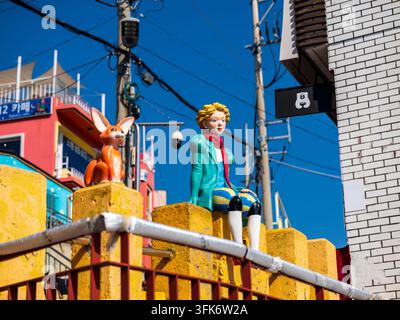 Busan, Corea del Sud - 14 febbraio 2026: Vista delle statue del Piccolo Principe e della volpe su un muro giallo nel villaggio culturale di Gamcheon, con edifici colorati Foto Stock