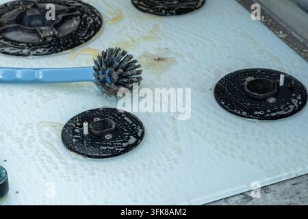 Una spazzola su un piano cottura in vetro bianco trattato con detergente Foto Stock
