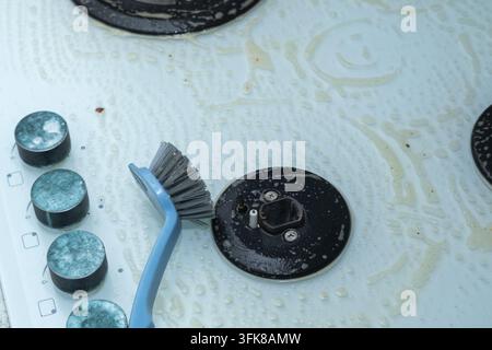 Una spazzola su un piano cottura in vetro bianco trattato con detergente Foto Stock