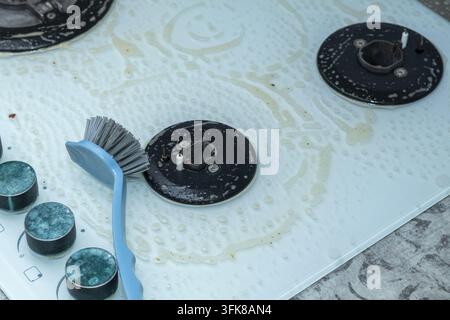 Una spazzola su un piano cottura in vetro bianco trattato con detergente Foto Stock