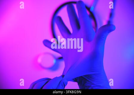 Mani di un operatore sanitario che indossano un guanto protettivo blu con uno stetoscopio alla luce al neon Foto Stock