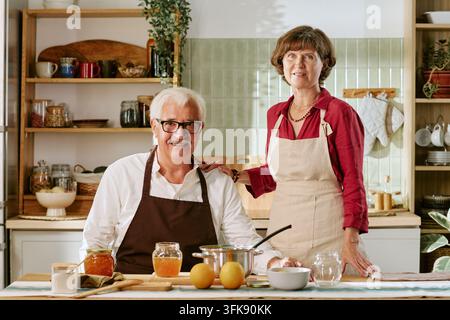Ritratto di una coppia anziana con grembiuli che prepara la marmellata in cucina Foto Stock