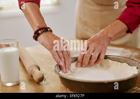 Donna anziana modella la pasta con le mani in una teglia per una torta fatta in casa Foto Stock