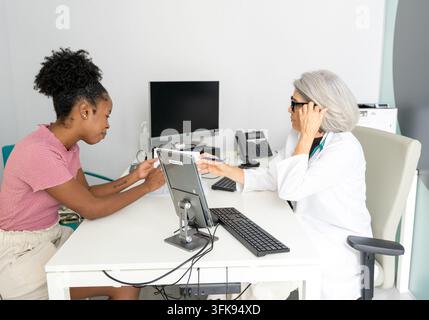 Medico che aiuta il paziente a compilare moduli medici digitali su un tablet in una clinica Foto Stock
