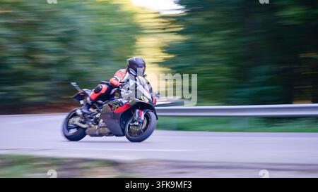 Moto sportiva inclinata in una curva stretta su una strada asfaltata tortuosa con sfondo sfocato dal movimento Foto Stock