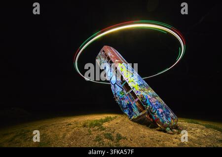 Un veicolo abbandonato dipinto in modo vivace si trova nella Foresta Internazionale delle Auto nel Nevada. Un anello di luce brillante creato da un drone circonda la scena unde Foto Stock