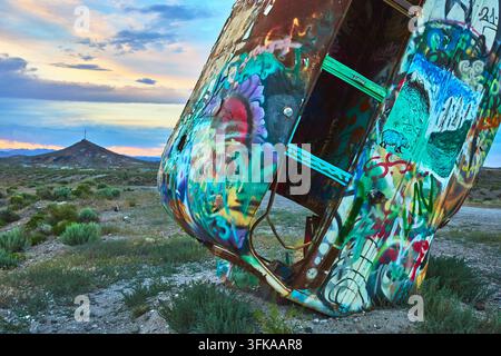 Un veicolo abbandonato dipinto in modo vivido si erge in piedi nel deserto del Nevada nella Foresta Internazionale delle Auto. L'arte graffiti e la luce dell'ora dorata creano una s Foto Stock