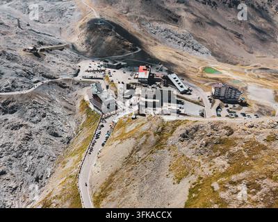 Vista aerea del Passo dello Stelvio con la strada di montagna tortuosa, le vette alpine circostanti, il terreno roccioso e gli edifici alla sommità a Stelvio, Trento Foto Stock