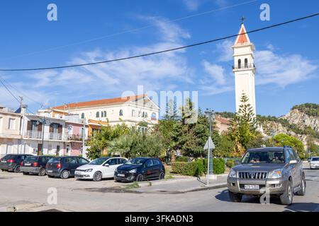 Città di Zante, Zacinto Grecia, 1° settembre 2026: Chiesa e alto campanile con croce accanto a una piazza cittadina e auto parcheggiate con alberi tradizionali Foto Stock