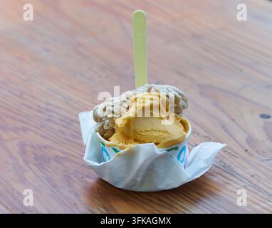 Cucchiaiate di gelato alla vaniglia e al cioccolato si trovano in una tazza di carta avvolta da un tovagliolo bianco, appoggiata su un piano di legno texture Foto Stock