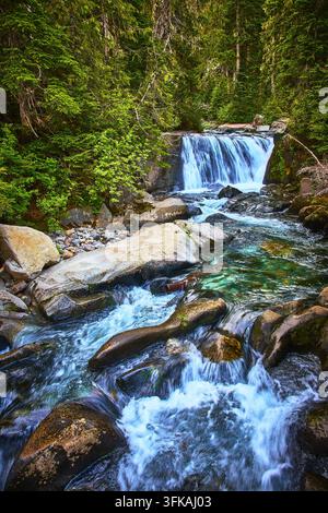 Cascata e ruscello che scorre attraverso una foresta in un paesaggio montano lussureggiante Foto Stock