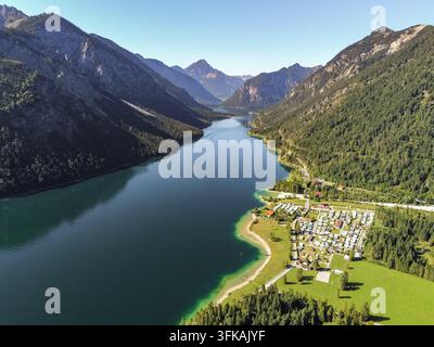 Vista aerea del lago Plansee circondato da montagne verdeggianti, foreste fitte e un campeggio sul lago nel distretto di Reutte, Tirolo, Austria. Foto Stock