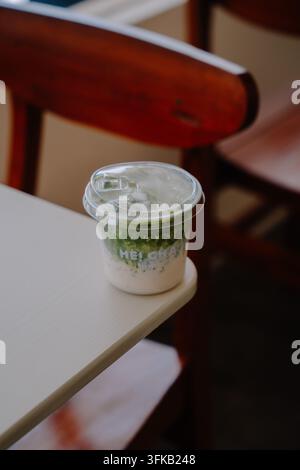 Latte freddo al tè verde matcha con latte in una tazza di plastica da asporto su un tavolo di legno nel caffè Foto Stock