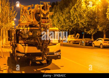 Gru mobile gialla parcheggiata sul ciglio della strada sotto i lampioni di notte Foto Stock