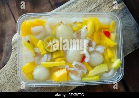 Asinan Kiamboy rinfrescante con fette di rambutan e mango in un contenitore trasparente guarnito con lime Foto Stock