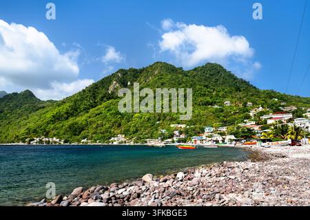 Bellissima costa del villaggio di Scotts Head con montagne verdi lussureggianti e una spiaggia di ciottoli lungo la baia di Soufriere a Dominica, Caraibi. Foto Stock