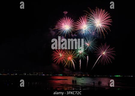 Fuochi d'artificio vivaci esplodono sull'oceano mentre folle si radunano sulla spiaggia per una celebrazione festiva a Pattaya, Thailandia. Foto Stock