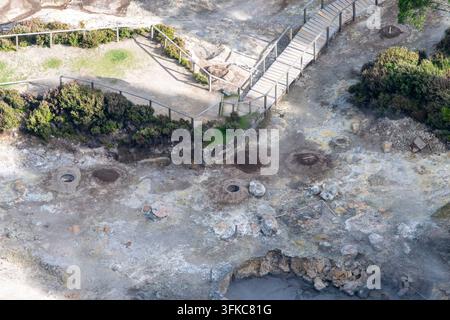 Fotografia aerea ad angolo elevato di un paesaggio geotermico aspro con una passerella di legno curva con ringhiere di sicurezza in metallo che si snoda attraverso i minerali- Foto Stock