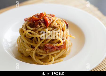 Spaghetti alti e attorcigliati con pomodorini confit e briciole di pane tostate su un piatto bianco, vista a 45 gradi, sfondo in stuoia di bambù Foto Stock