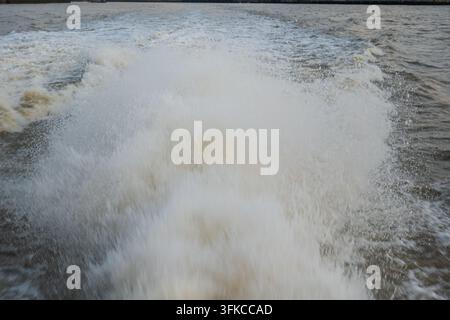 Vista ravvicinata di spruzzi d'acqua bianchi densi, schiuma e risacca agitata generata da un motore di barca ad alta velocità che si muove rapidamente sull'acqua del fiume sotto una leggera Foto Stock