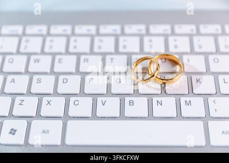 Fedi nuziali d'oro posate su una tastiera del computer, rappresentanti la pianificazione del matrimonio online, i servizi di matrimonio digitali, le prenotazioni su Internet, i siti web di matrimonio a Foto Stock