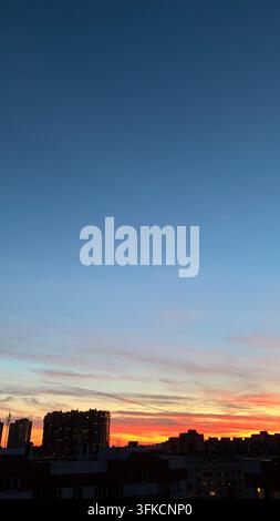 Scatto verticale all'aperto di un drammatico cielo al tramonto colorato che passa dal blu profondo all'arancione brillante sopra le silouette scure di edifici residenziali urbani Foto Stock