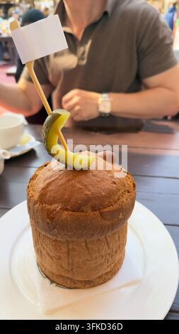 Scatto verticale interno di una presentazione creativa di cibo con pane rotondo cotto su un piatto bianco con uno stuzzicadenti di legno che tiene una fetta di cetriolo e emp Foto Stock
