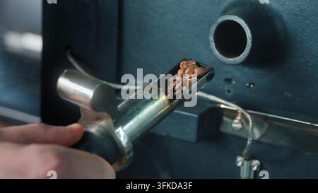 Mano di un operaio maschile irriconoscibile che preme una leva su una macchina per la tostatura del caffè alla bocca di fabbrica, rilasciando chicchi e mescolando cereali durante la produzione Foto Stock