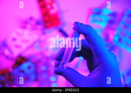 Mano guantata che tiene una provetta con liquido durante un esperimento scientifico Foto Stock