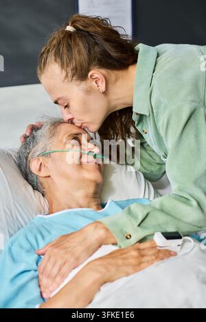 Donna che bacia la fronte di un paziente anziano in ospedale sostenendo la guarigione Foto Stock